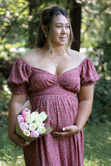 woman wearing a patterned off-the-shoulder maternity dress and holding a bouquet of tulips while cradling her baby bump