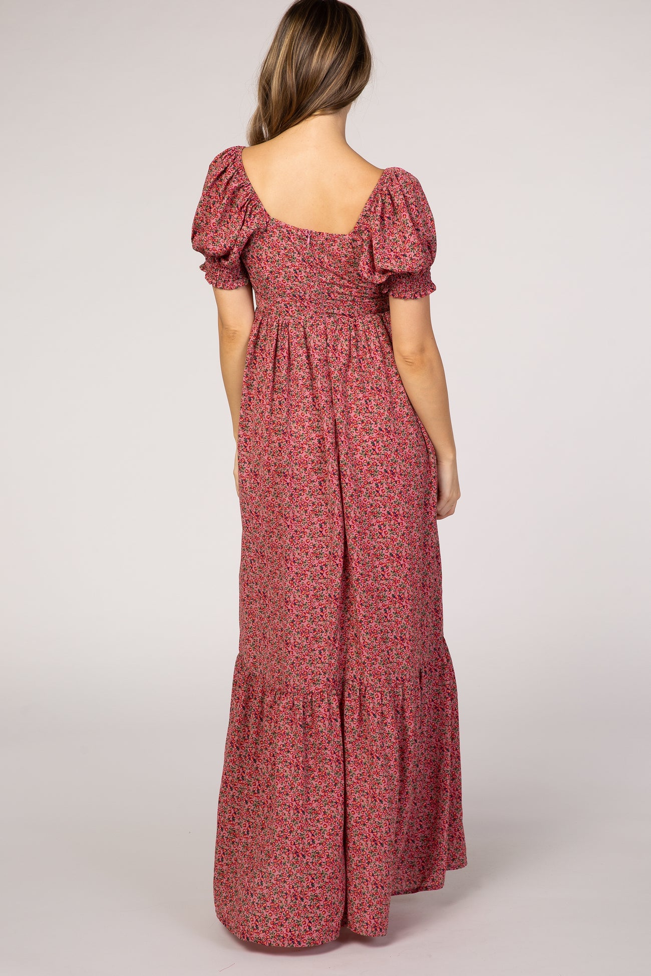 woman wearing a pink floral maternity maxi dress with puff sleeves and a ruffled hem, showing the back view