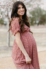 woman wearing a floral pink maternity dress and showing her baby bump outdoors