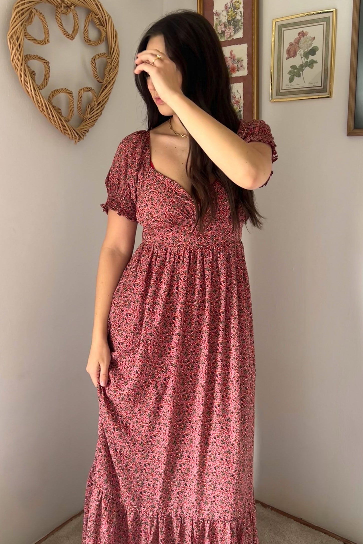 woman wearing a pink floral maxi dress with puff sleeves and a ruffled hem, posing with one hand on her face