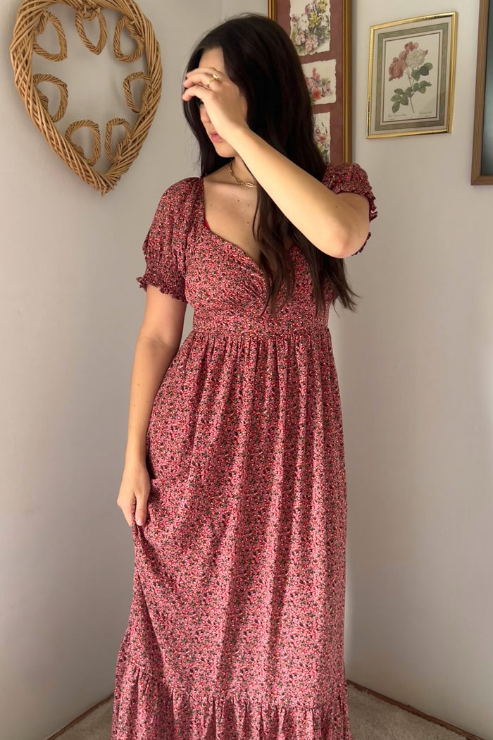 woman wearing a pink floral maxi dress with puff sleeves and a ruffled hem, posing with one hand on her face