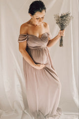 woman wearing a blush pink off-the-shoulder maternity dress holding her baby bump and a bouquet of dried flowers