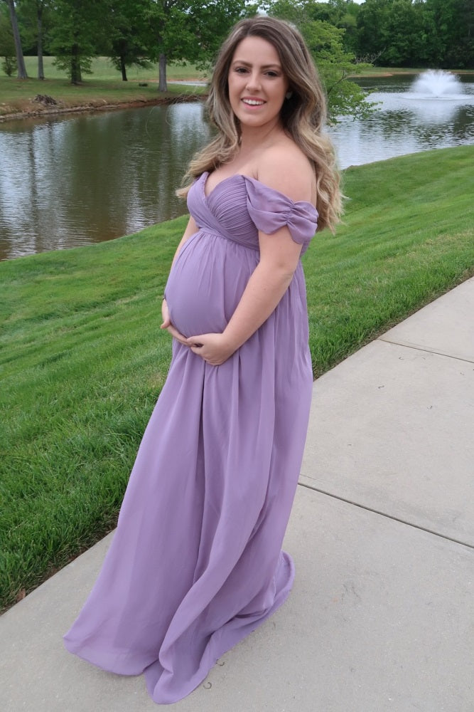 woman wearing a lavender off-the-shoulder maternity gown while holding her baby bump by a pond