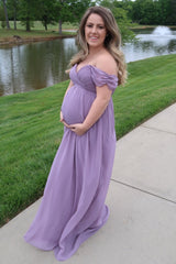 woman wearing a lavender off-the-shoulder maternity gown while holding her baby bump by a pond