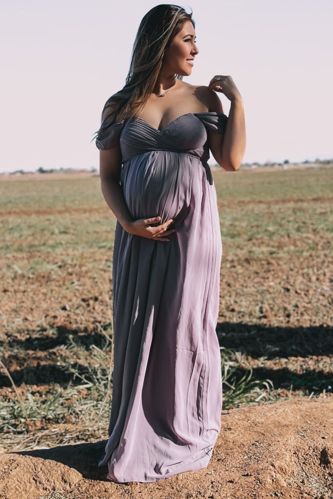 woman wearing a lavender off-the-shoulder maternity gown and holding her baby bump in a field