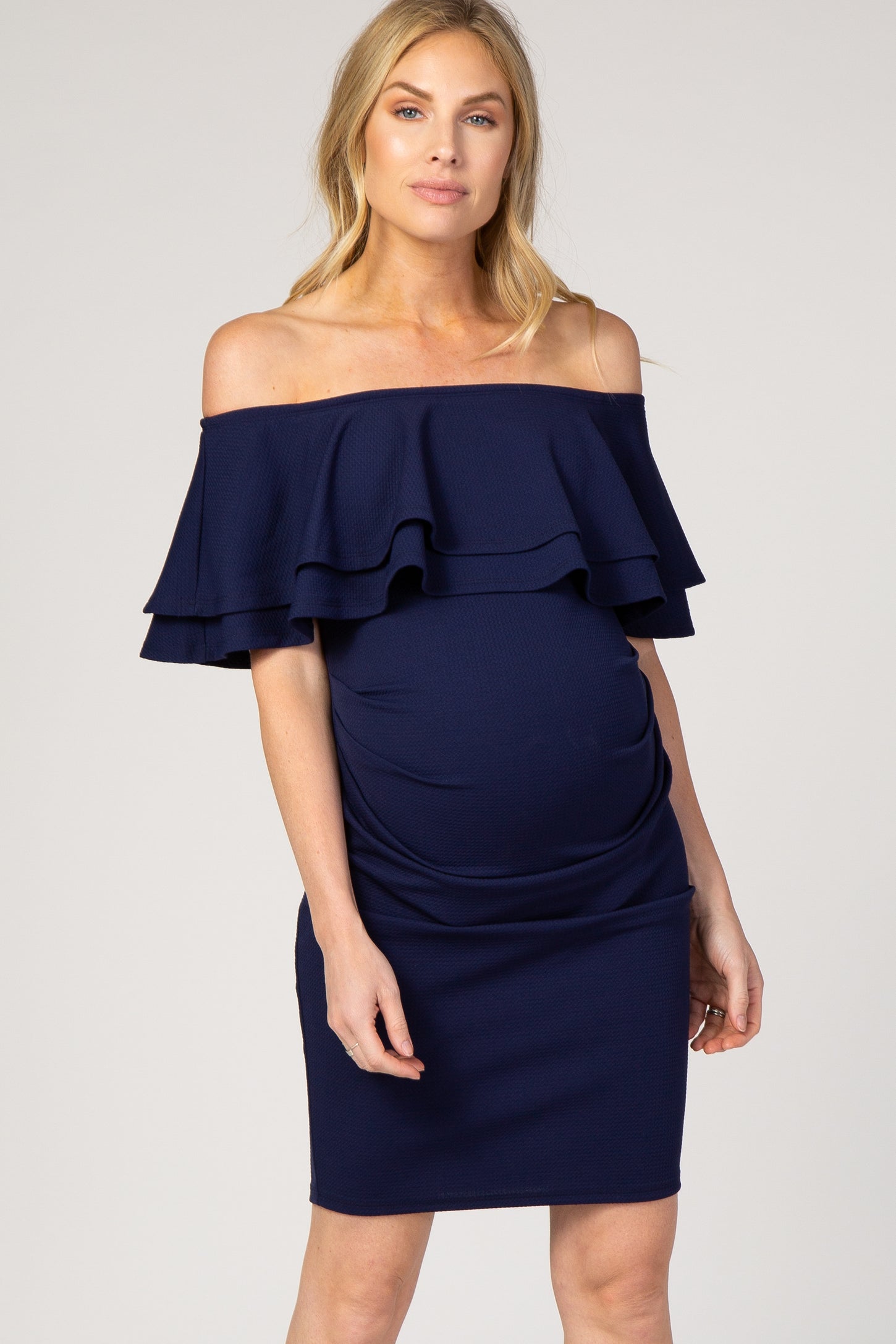 Pregnant woman wearing a navy blue off-the-shoulder maternity dress with tiered ruffles