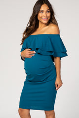 woman wearing a teal off-the-shoulder maternity dress with ruffle details and holding her baby bump