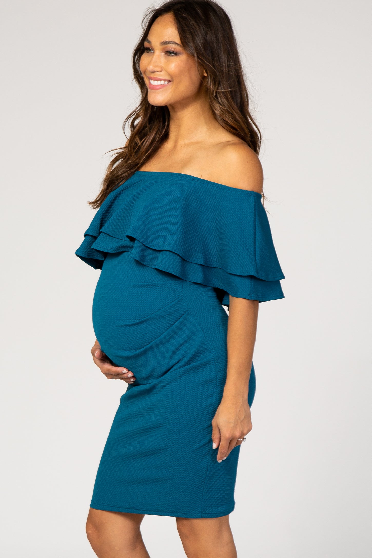 woman wearing a teal off-the-shoulder maternity dress with ruffle details and a visible baby bump