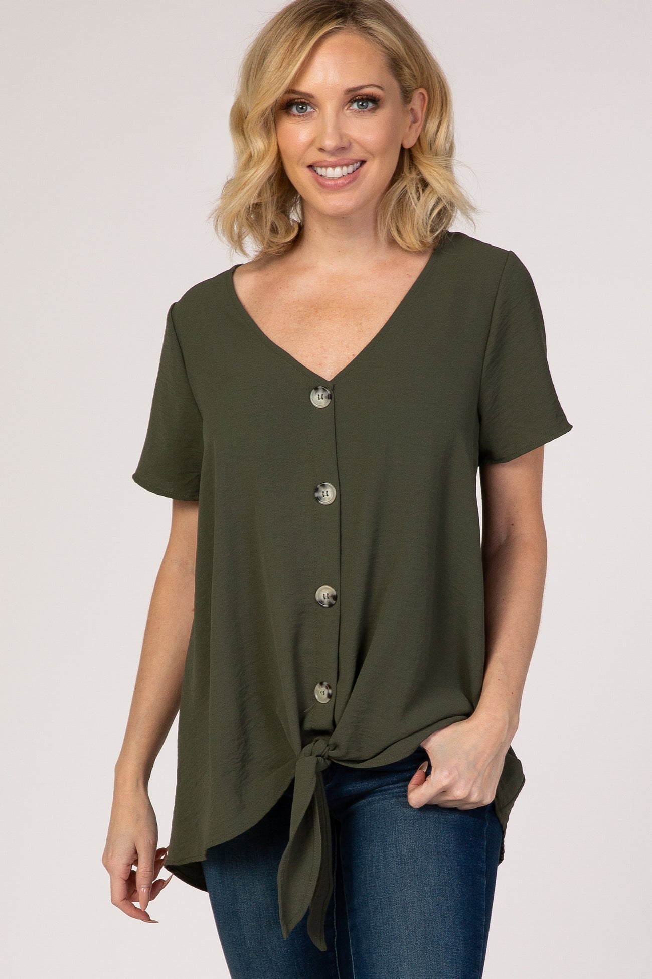 woman wearing an olive green short sleeve button down top with a front tie hem and blue jeans