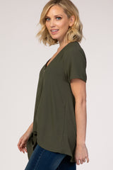 woman wearing an olive green short sleeve top with a v-neck and side tie detail, paired with blue jeans