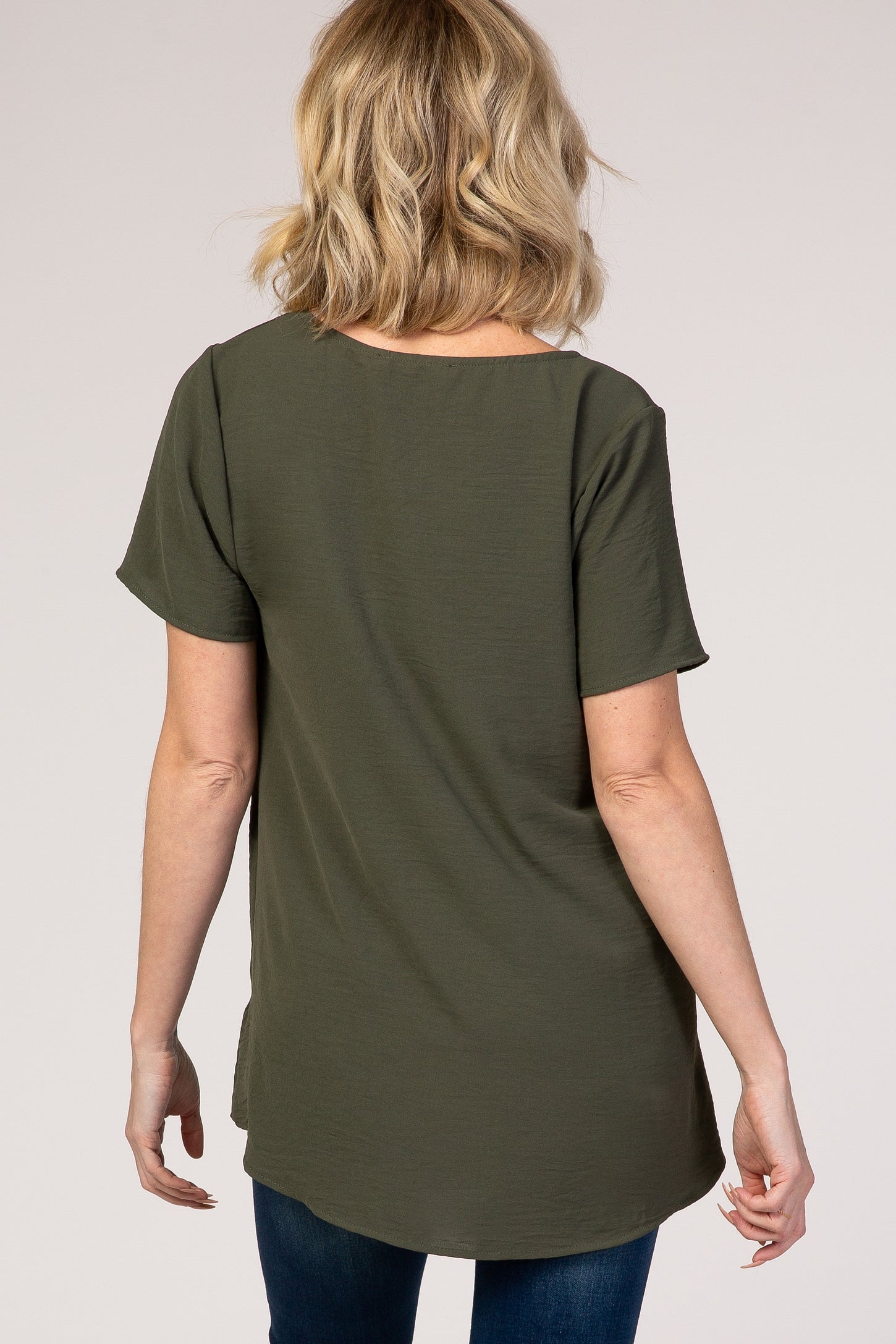 woman wearing a dark green short sleeve top with a curved hem and relaxed fit, viewed from the back