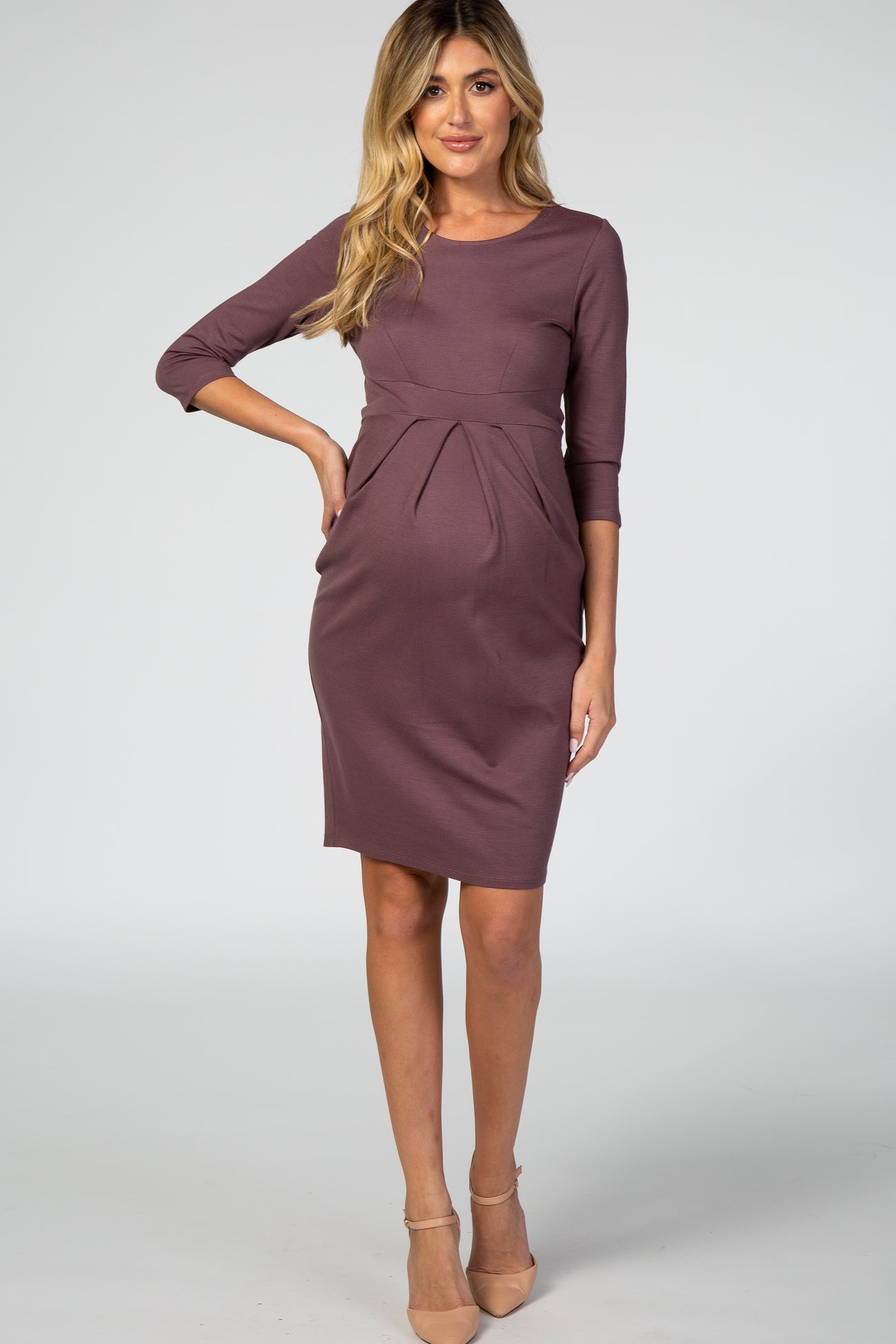 woman wearing a mauve maternity dress with three-quarter sleeves and a pleated detail over her baby bump