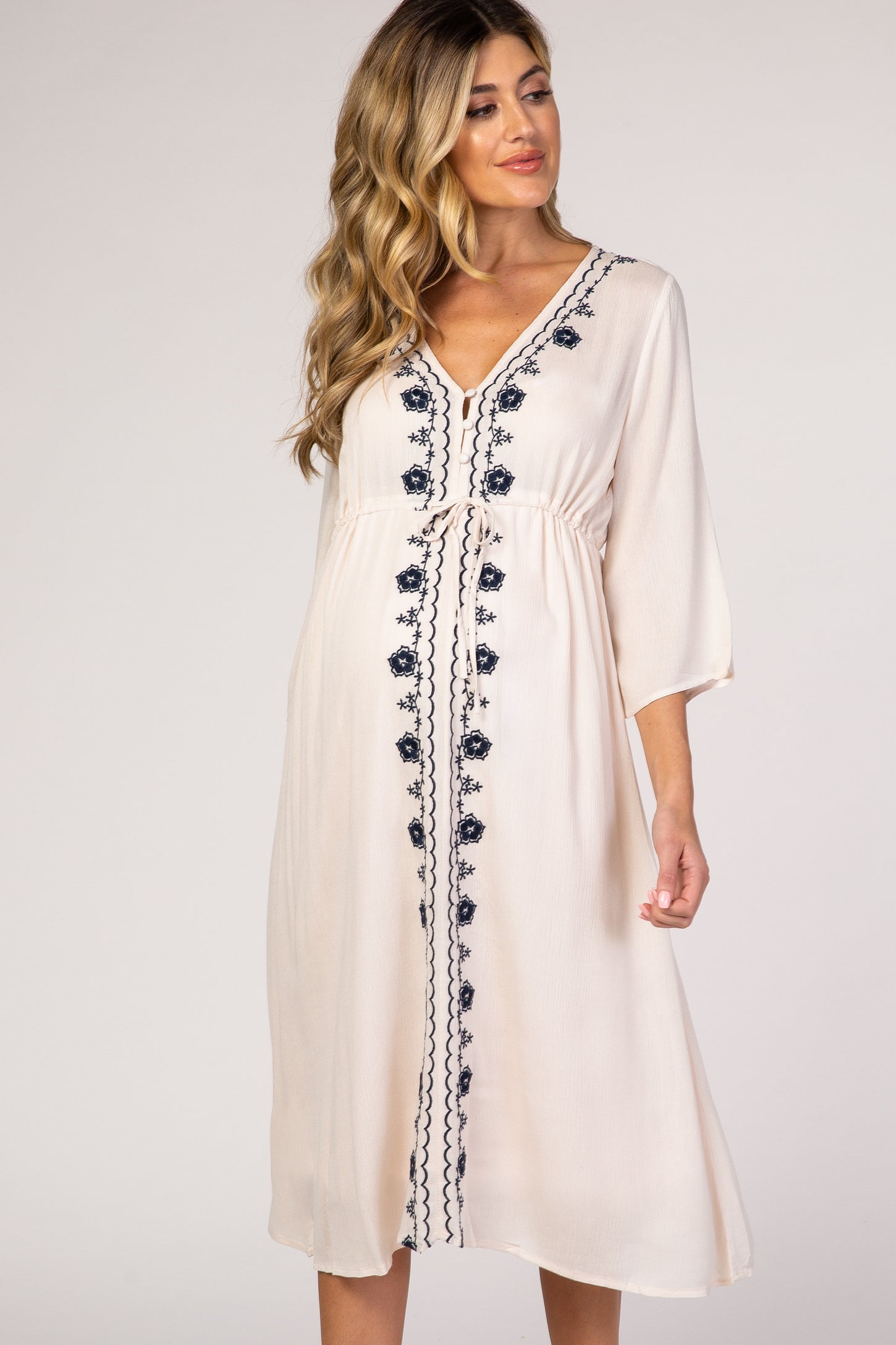 pregnant woman wearing cream maternity midi dress with navy blue floral embroidery and drawstring waist