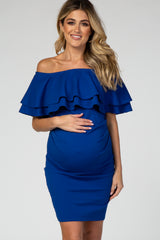 woman wearing a royal blue off-the-shoulder maternity dress with layered ruffles and holding her baby bump