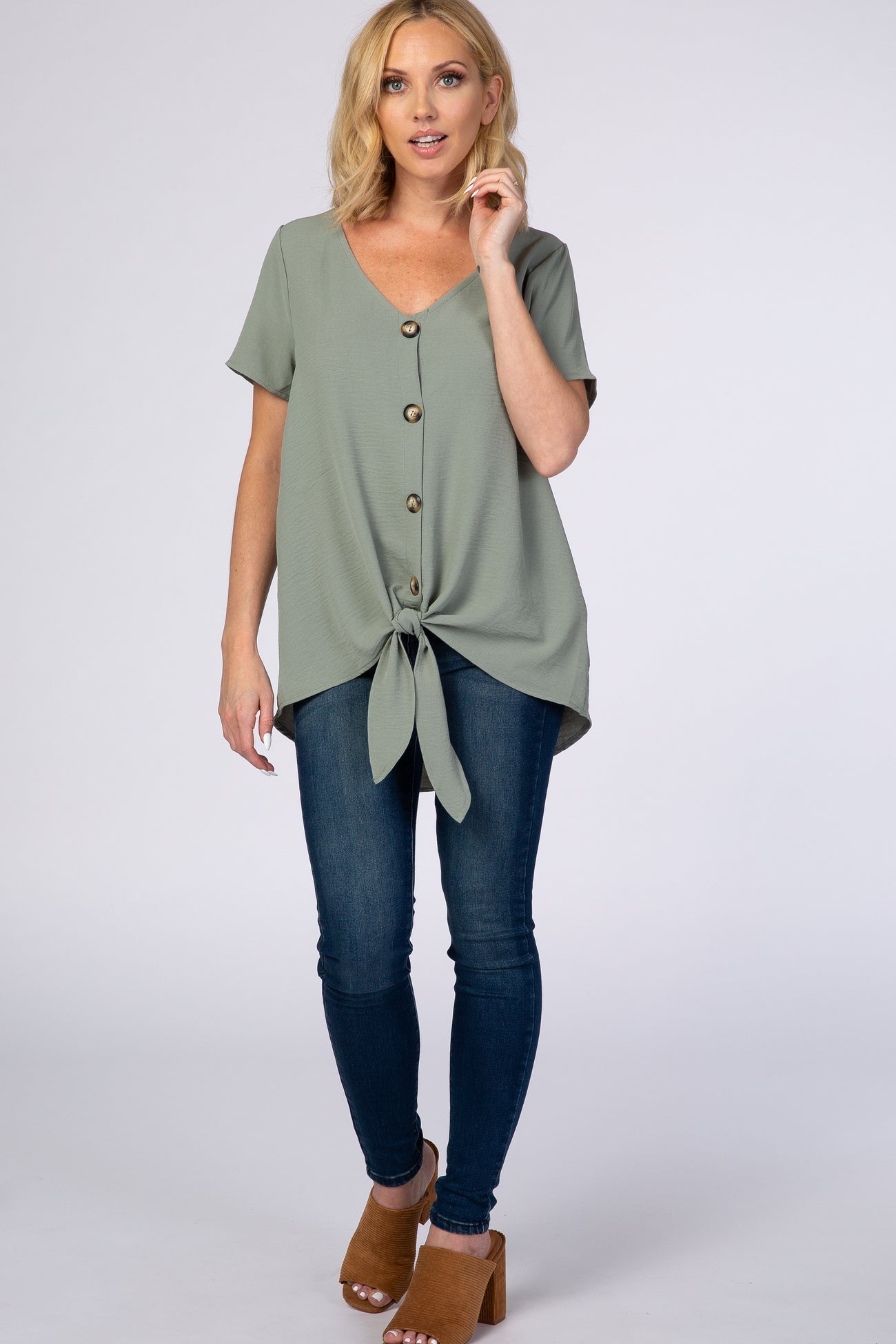 woman wearing sage green button down tie front top and dark wash skinny jeans with brown mule heels