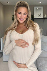 woman wearing a beige ribbed maternity dress and holding her baby bump, smiling at the camera