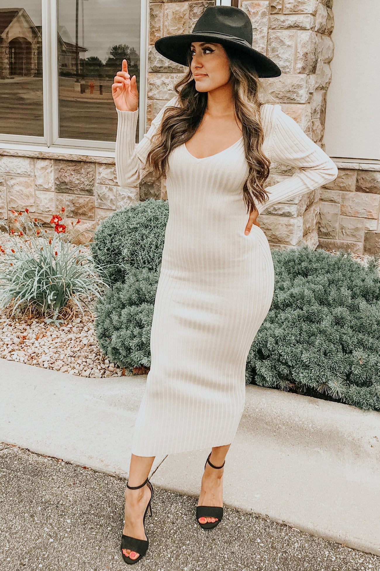 woman wearing a ribbed cream knit maxi dress and a black wide-brimmed hat, posing outdoors with a stylish stance