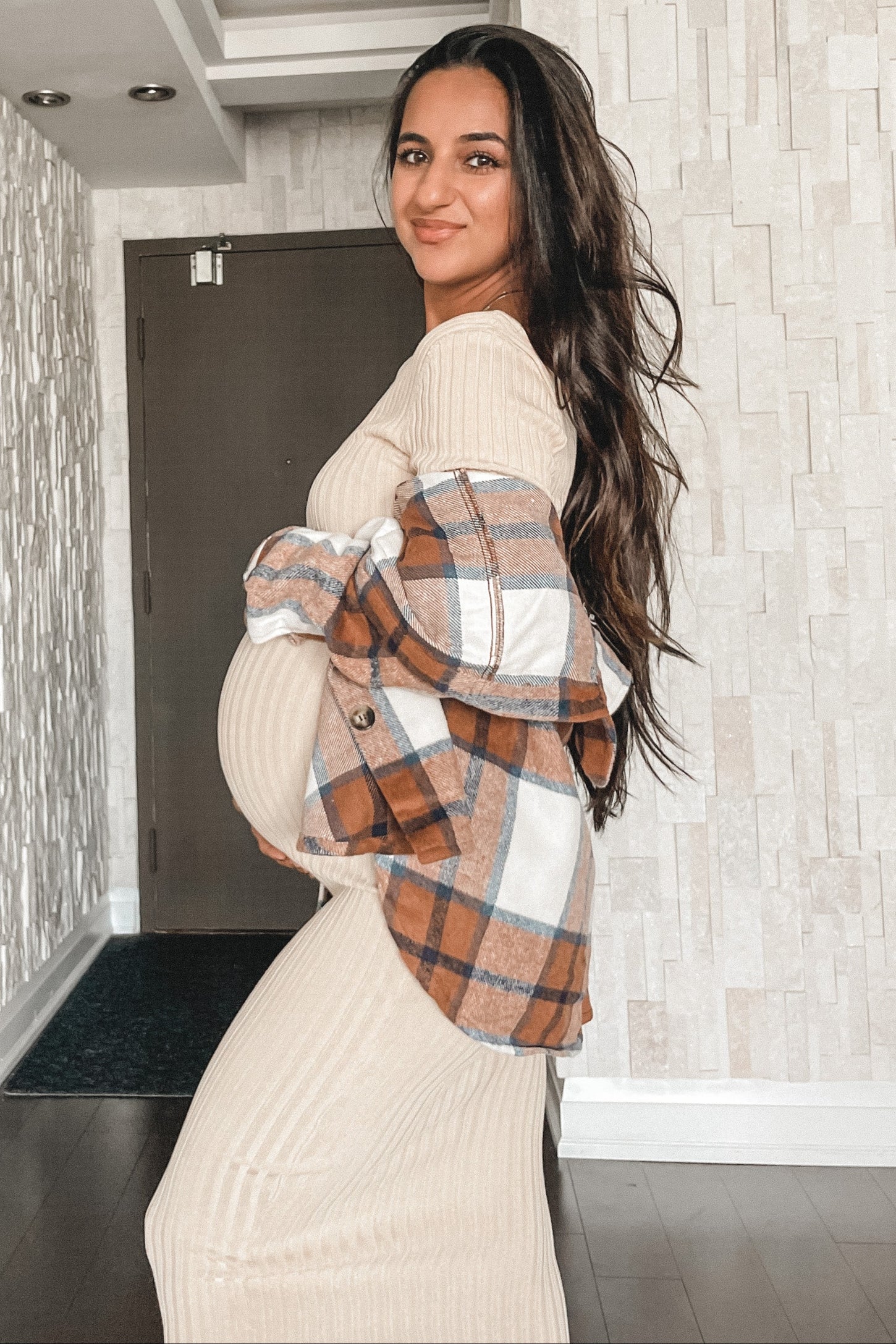 woman wearing a beige ribbed maternity dress and a plaid oversized jacket, showing her baby bump