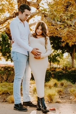 woman wearing a cream ribbed maternity dress with a baby bump, standing with a man in a white shirt and jeans