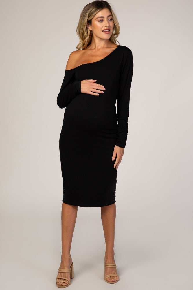 woman wearing a black one-shoulder maternity dress and holding her baby bump