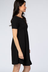 woman wearing a short sleeve black maternity dress with pleated skirt shown from a side profile view