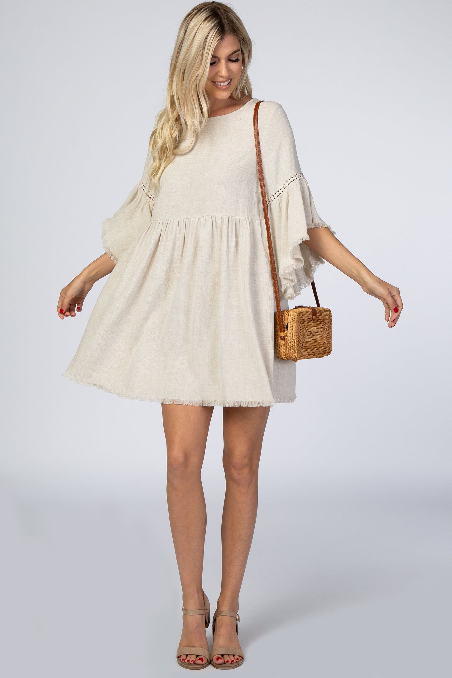 woman wearing a light beige swing dress with ruffled sleeves and a frayed hem, holding a small woven handbag