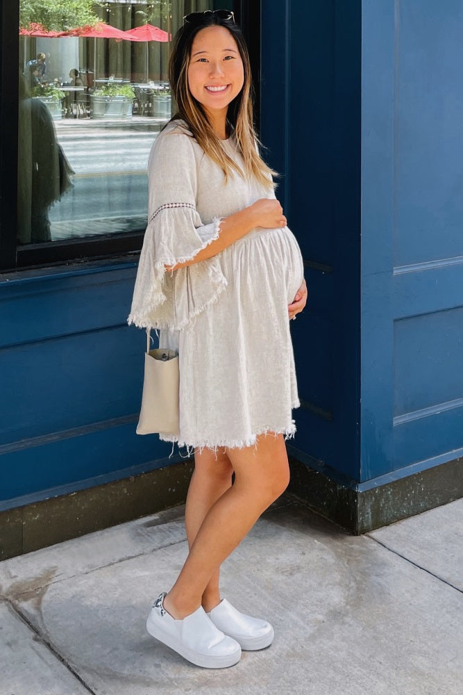 woman wearing a beige maternity dress with bell sleeves and a visible baby bump, smiling outdoors