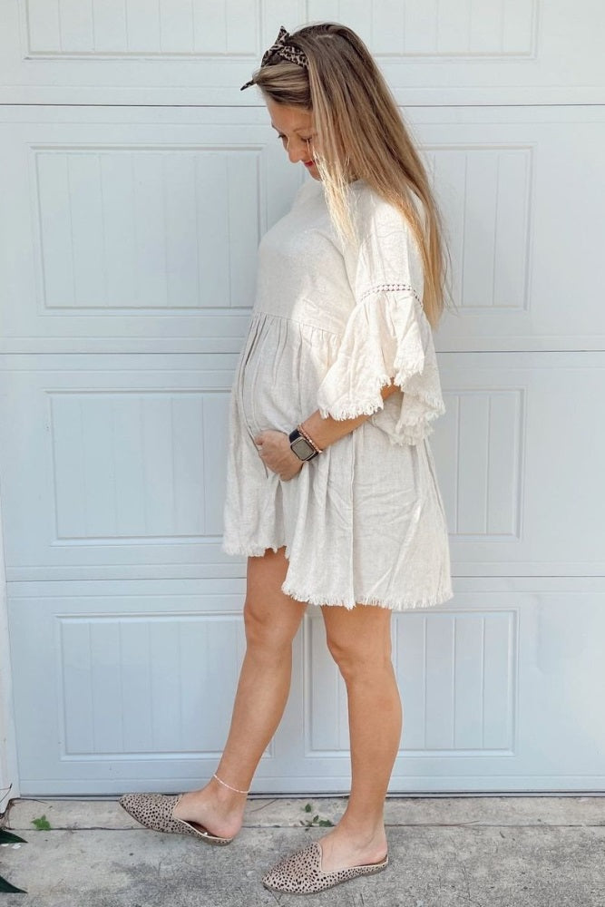 woman wearing a light beige short sleeve maternity dress with lace details and a visible baby bump