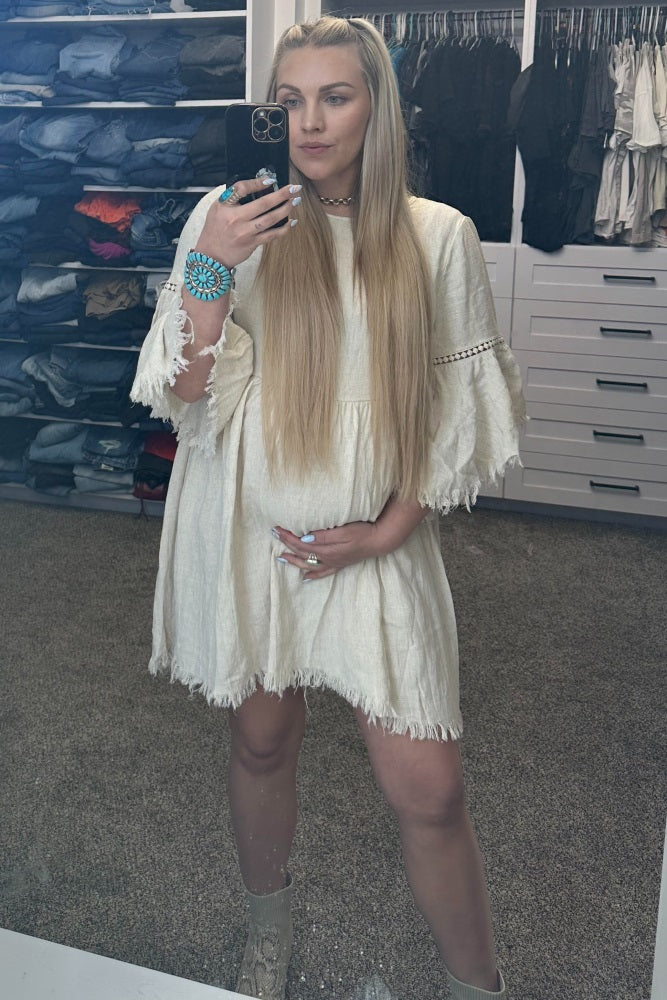 pregnant woman in cream fringe dress taking mirror selfie in walk-in closet with turquoise jewelry