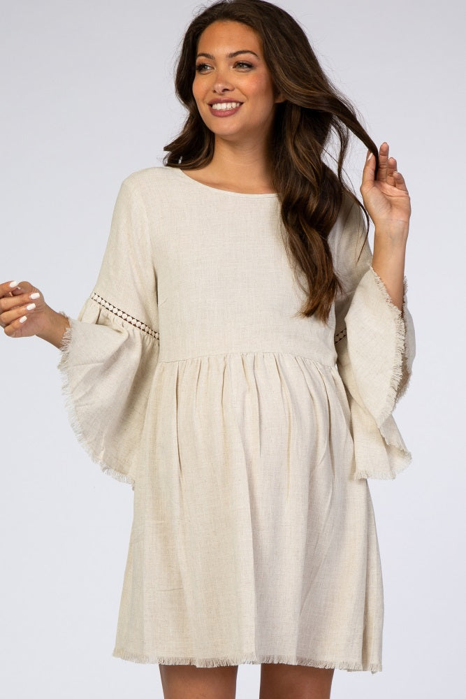 woman wearing a beige maternity dress with bell sleeves and a frayed hem, showing her baby bump