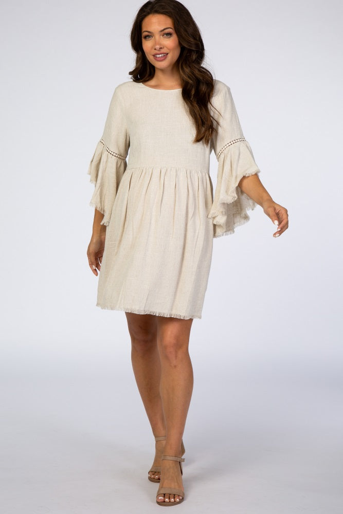woman wearing a cream maternity dress with wide sleeves and fringe hemline, walking gracefully