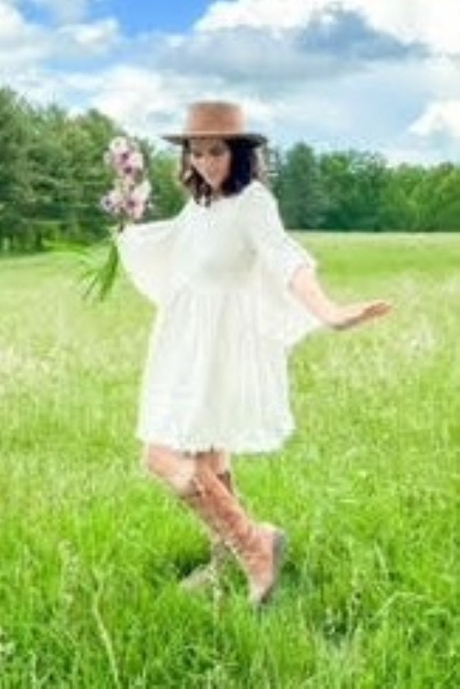woman wearing a white maternity dress with bell sleeves, holding flowers, standing in a grassy field