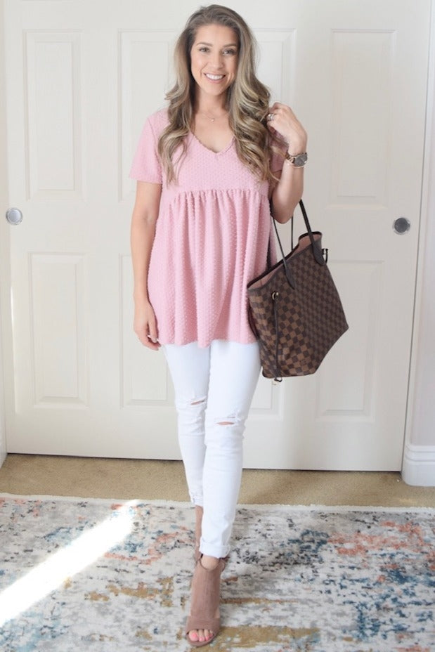 woman wearing a pink polka dot peplum top with white distressed skinny jeans and holding a brown patterned tote bag