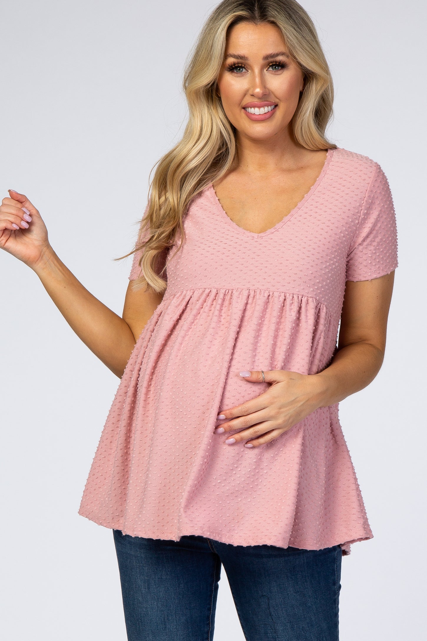 woman wearing a light pink maternity top with short sleeves and a v-neck, cradling her baby bump