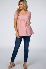 woman wearing a light pink short sleeve maternity top with textured dots and a baby bump, paired with dark skinny jeans