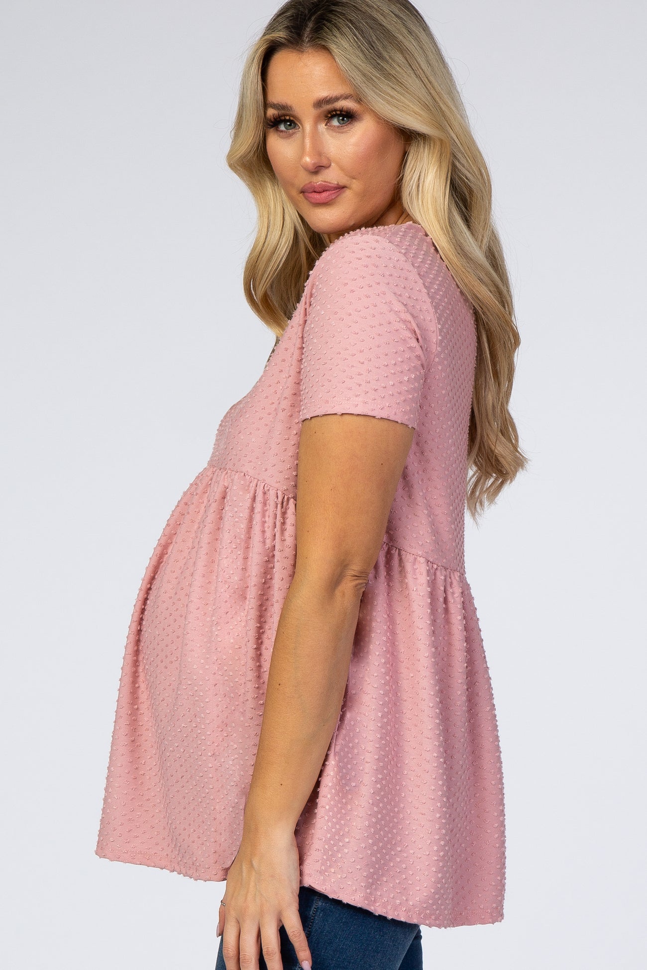 woman wearing a light pink short sleeve maternity top with textured dot detail and a visible baby bump