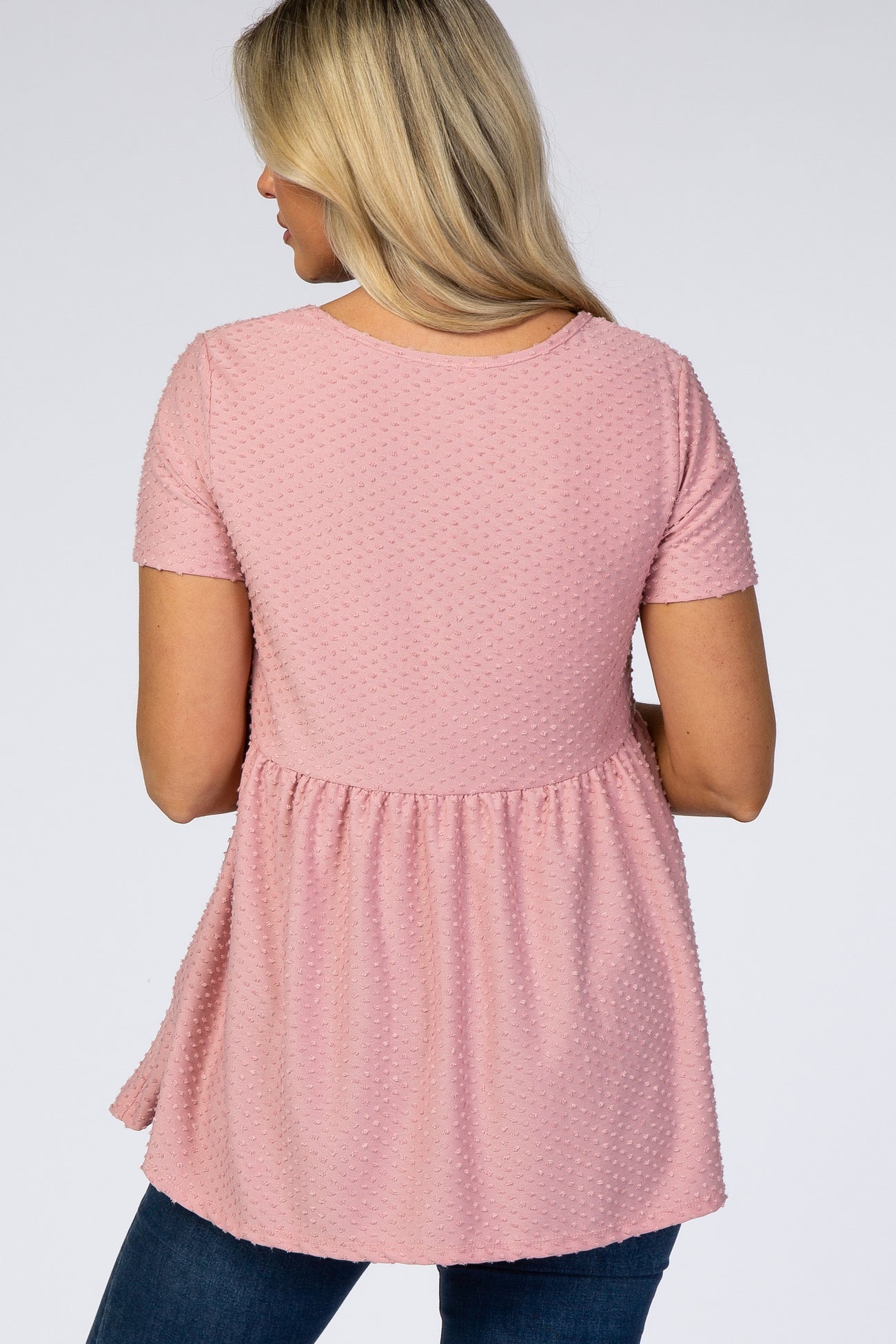 woman wearing a light pink short sleeve maternity top with textured fabric and a relaxed babydoll fit, showing her back