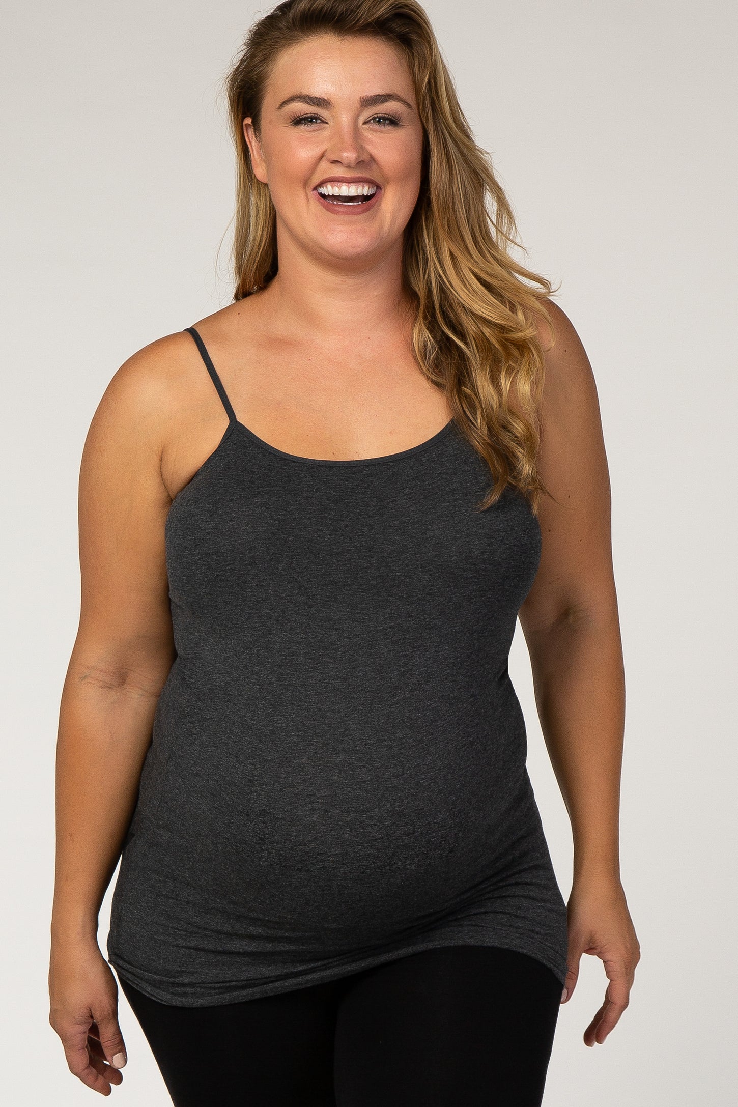 woman wearing a dark gray maternity tank top with thin straps and a visible baby bump, smiling and standing confidently