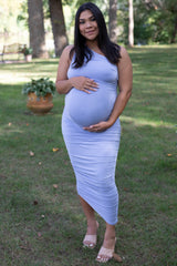 woman wearing a light lavender maternity dress, cradling her baby bump in a grassy outdoor setting