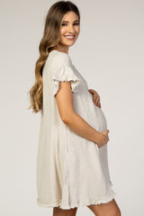 Smiling pregnant woman wearing a beige linen maternity dress with frayed ruffle sleeves and hem