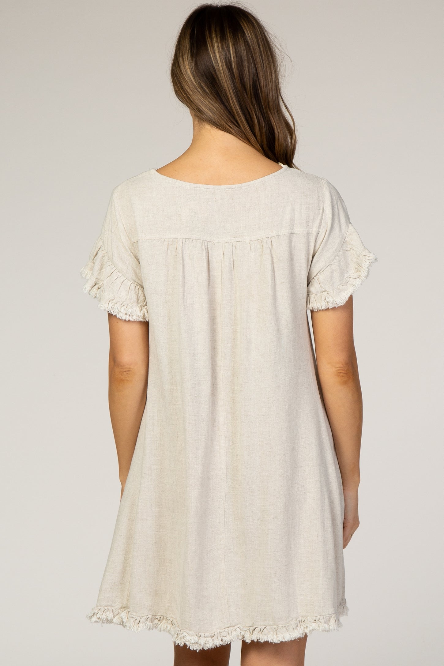 woman wearing a cream-colored maternity dress with ruffled short sleeves, showing a relaxed fit and a gathered back design