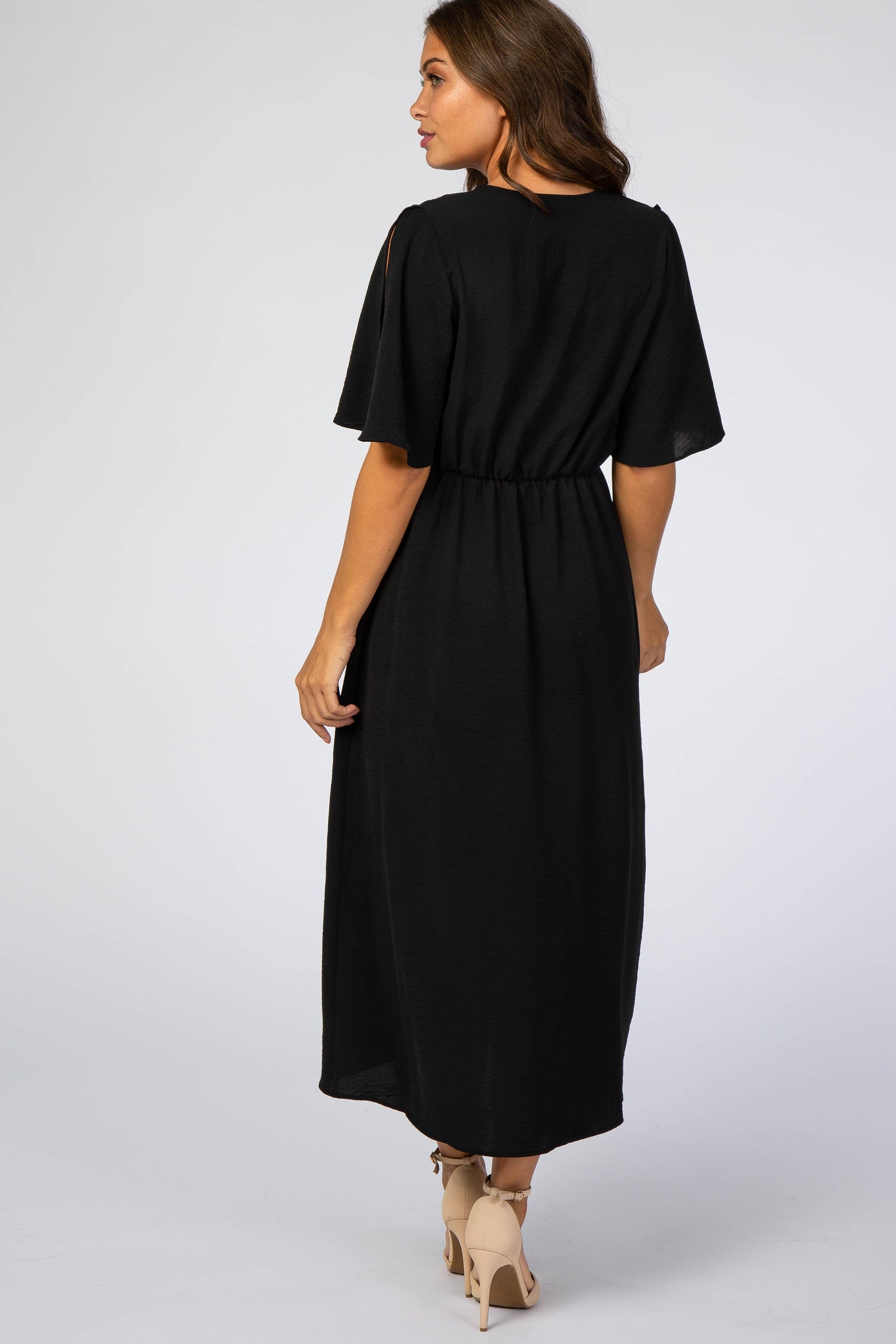 Back view of a woman wearing a black short sleeve midi dress with an elastic waist and beige heels