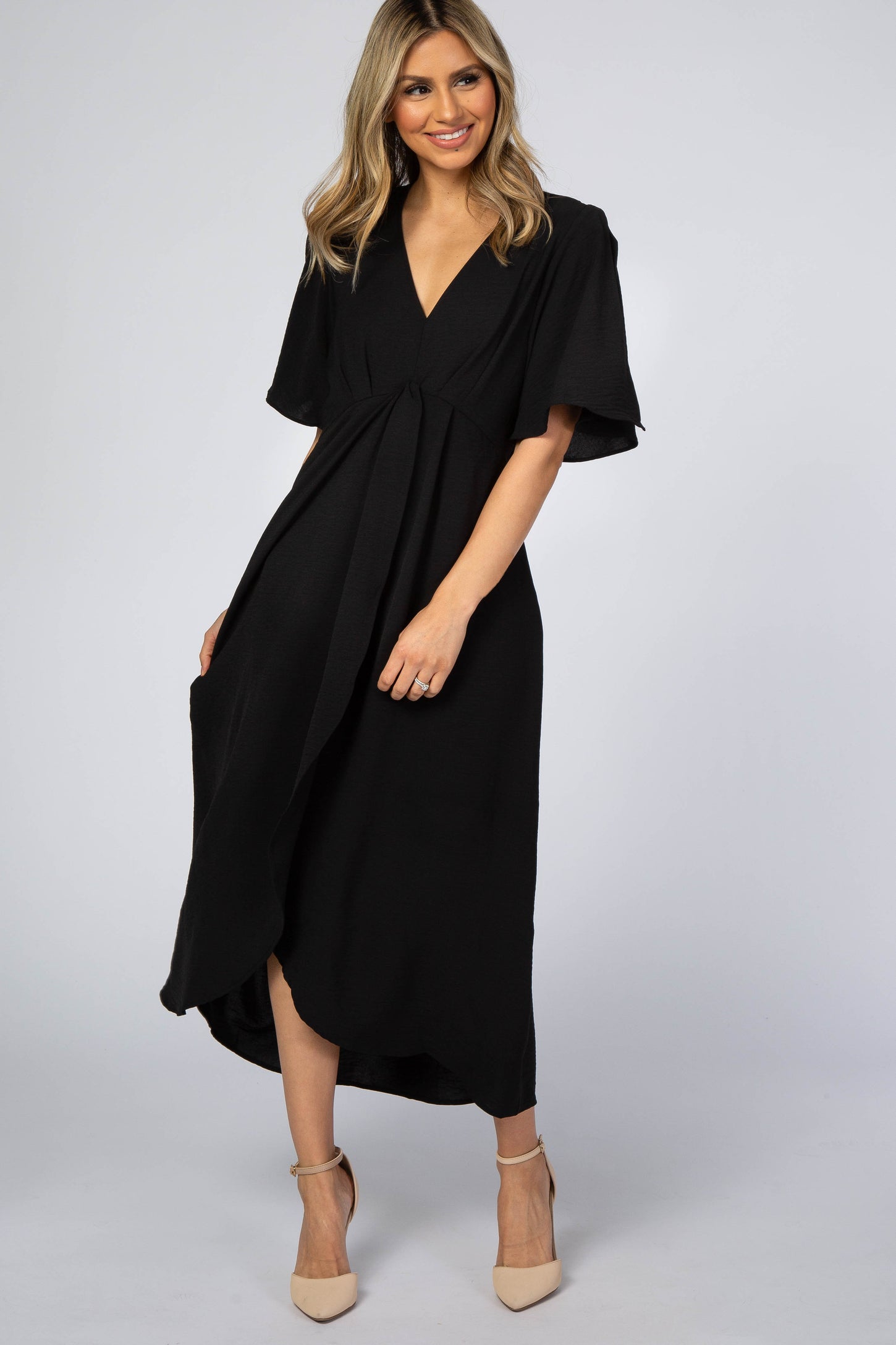 woman wearing a black wrap dress with short flutter sleeves and a deep v-neckline, standing in a model pose