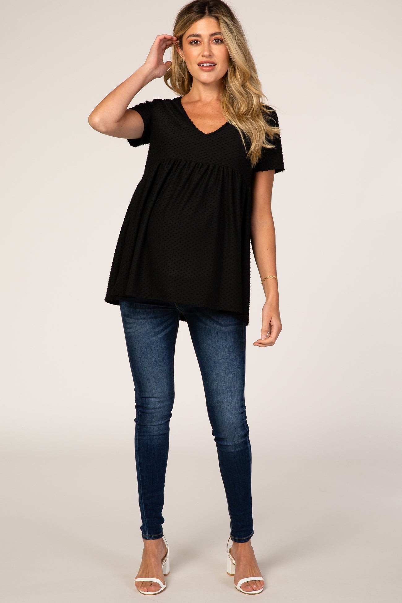 woman wearing a black short sleeve maternity top with a v-neck and flowing bottom, paired with blue skinny jeans