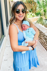 woman wearing a light blue sleeveless maxi dress and holding a newborn in matching blue outfit and headband
