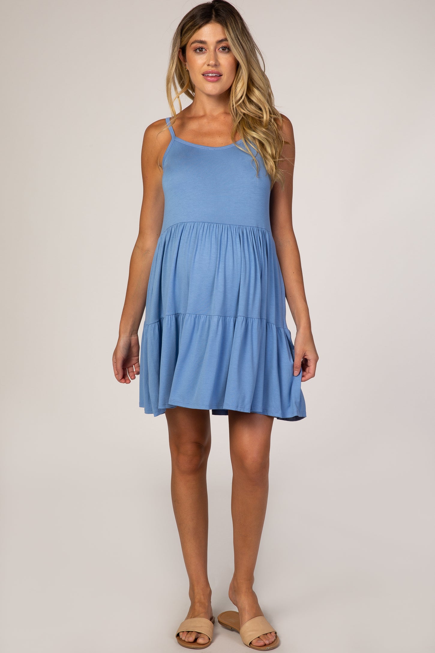 woman wearing a light blue maternity dress with a tiered skirt and adjustable straps, showcasing her baby bump