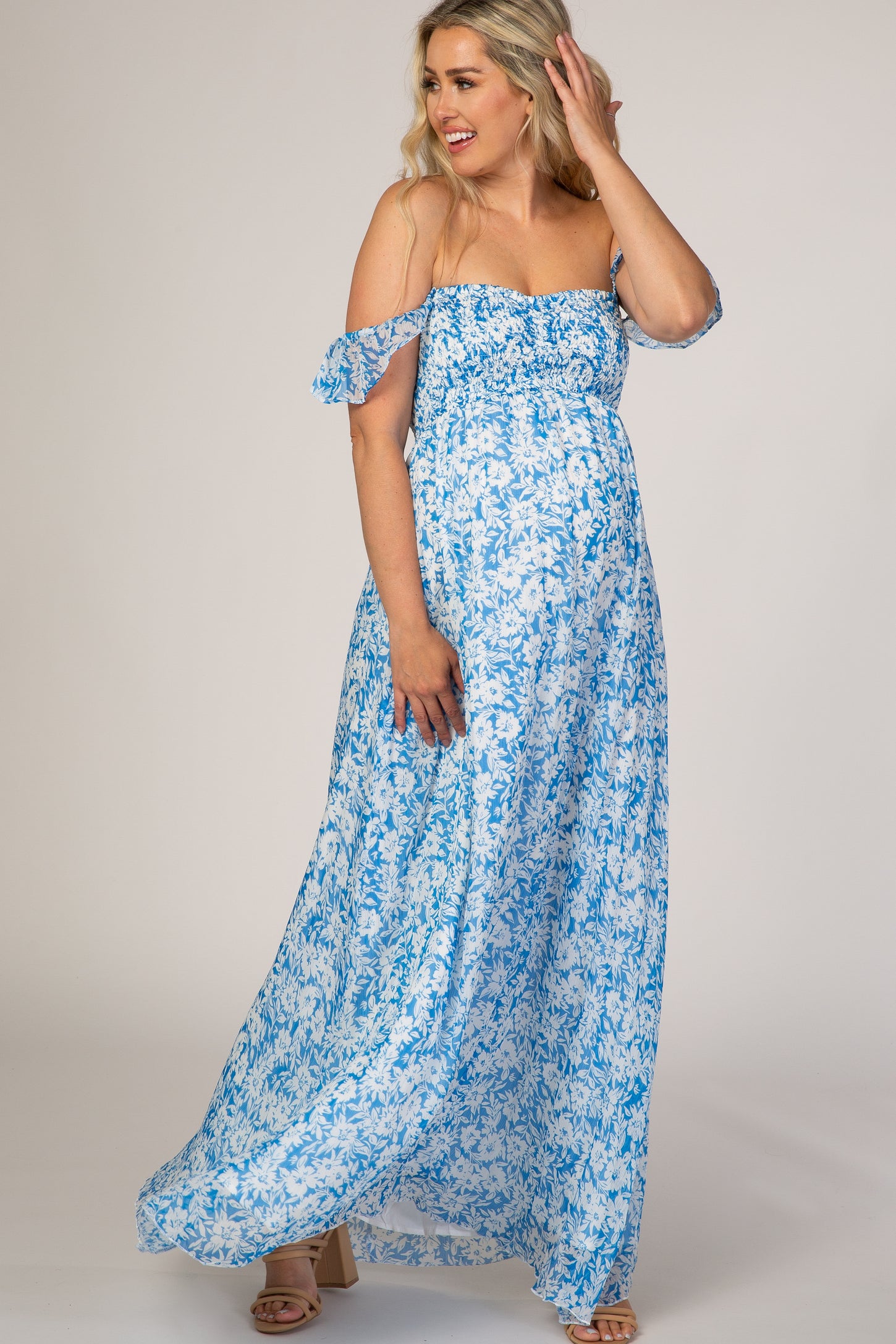 woman wearing a light blue floral off-shoulder maternity maxi dress with a smocked bodice and flowing skirt, baby bump visible