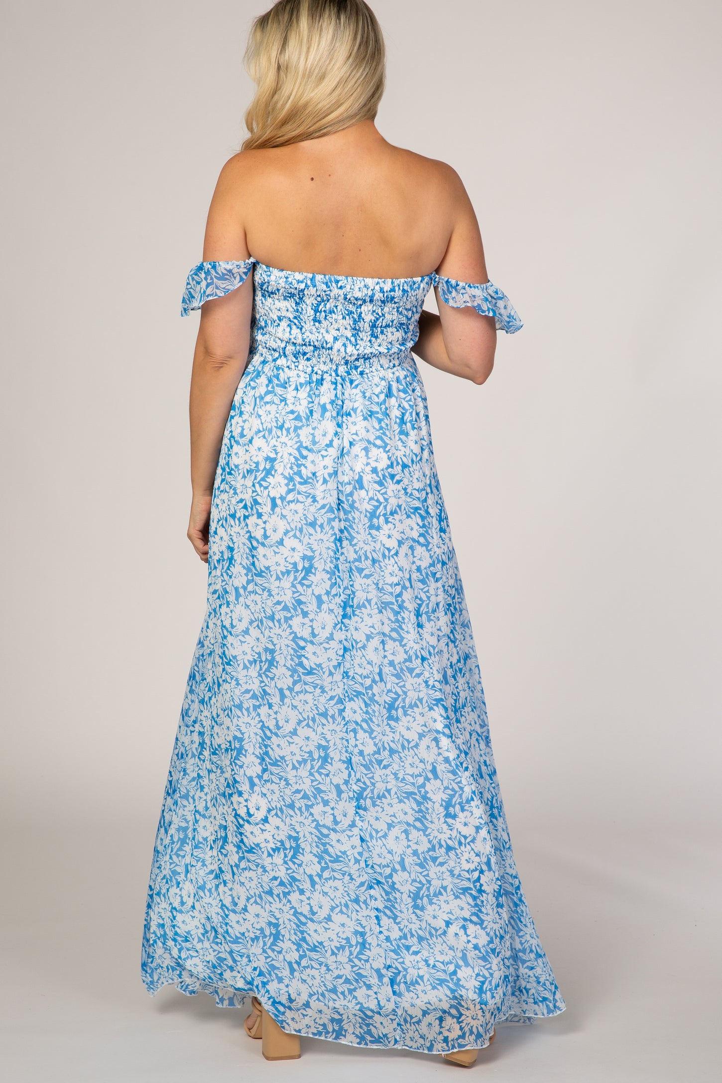 woman wearing a light blue off-the-shoulder floral maternity maxi dress, showing a flowing back view