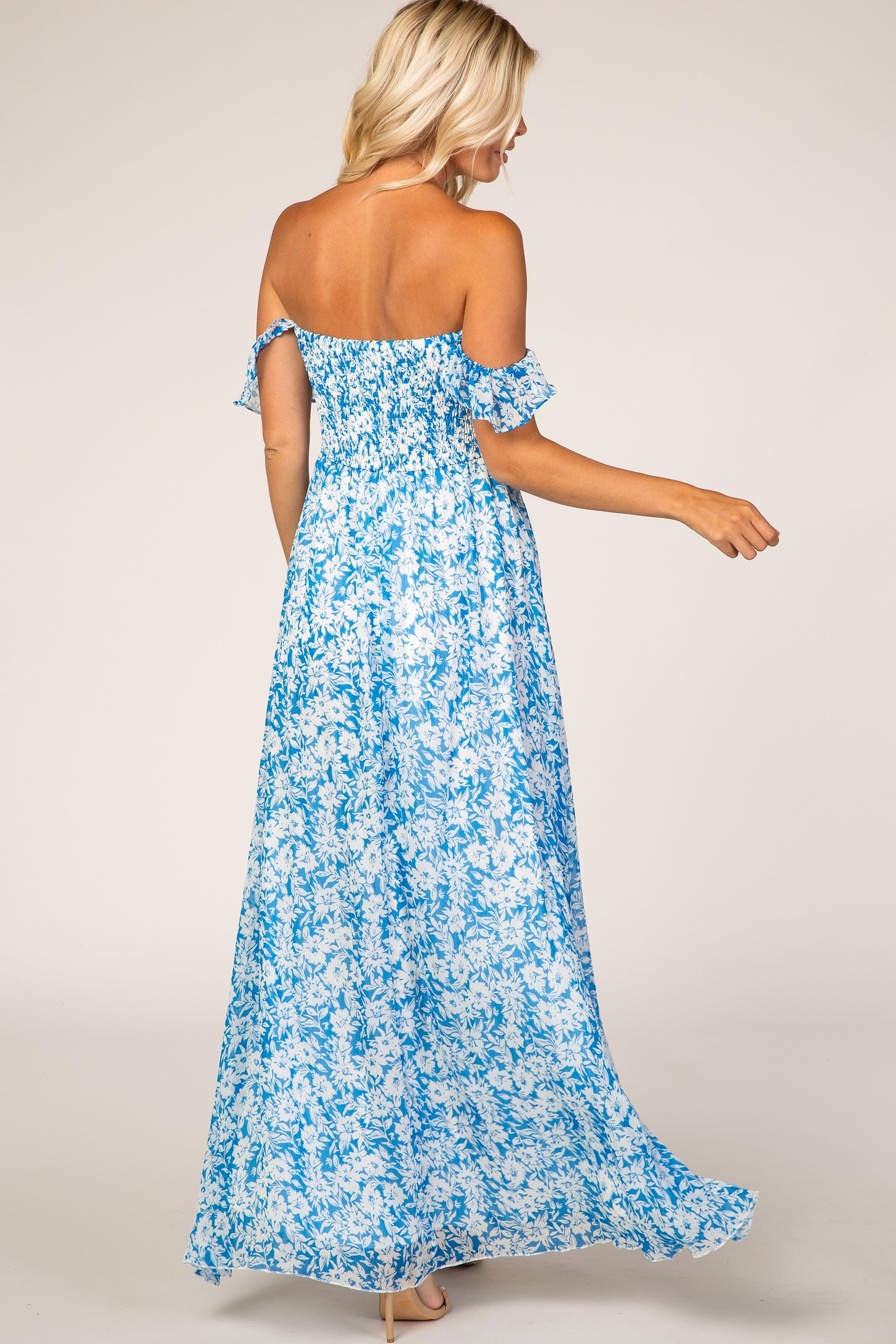 woman wearing a blue and white floral off-the-shoulder maxi dress, seen from the back, flowing fabric and ruffled sleeves