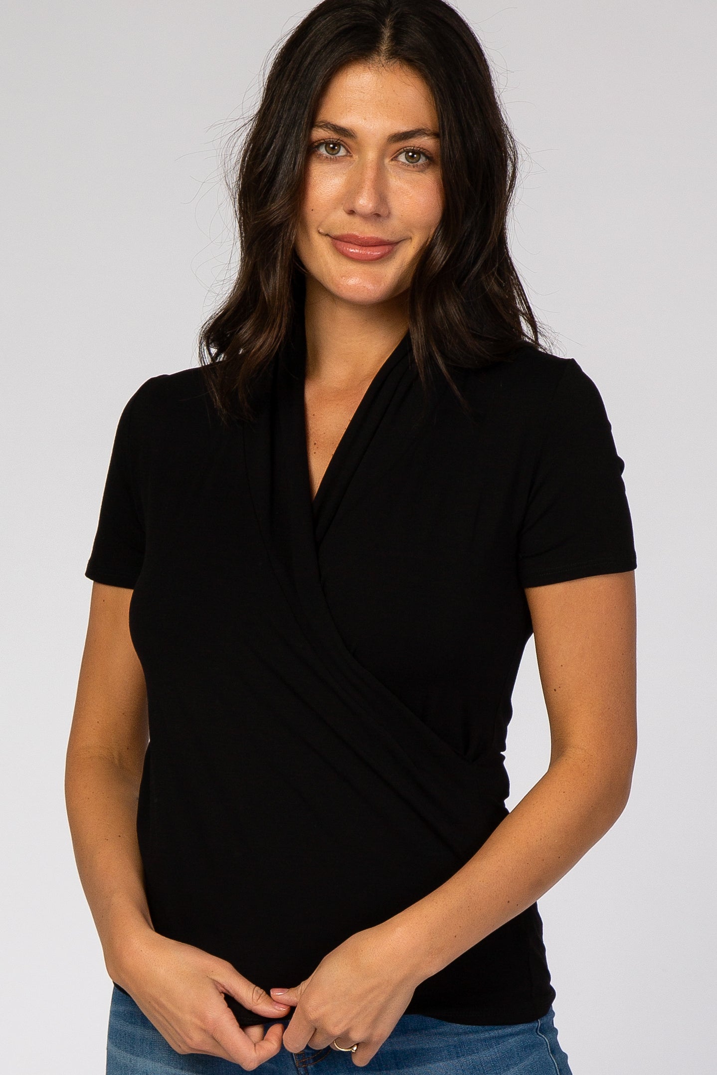 woman wearing a black short sleeve wrap top, smiling and posing with her hands on her waist